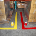 Loading zones in a warehouse marked with red and yellow tape installed with floor marking tape applicator