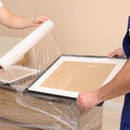 Individual wrapping up a picture frame  with stretch wrap packaging plastic film