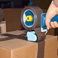 Individual showing hand-held tape dispenser application on brown shipping box