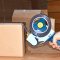Individual showing hand-held tape dispenser application on brown shipping box